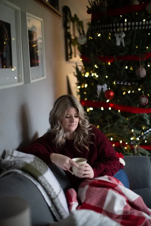 Libby Ward sits on a sofa holding a mug looking sad in front of a Christmas tree