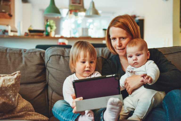 Mother sites on sofa with two children while looking at tablet