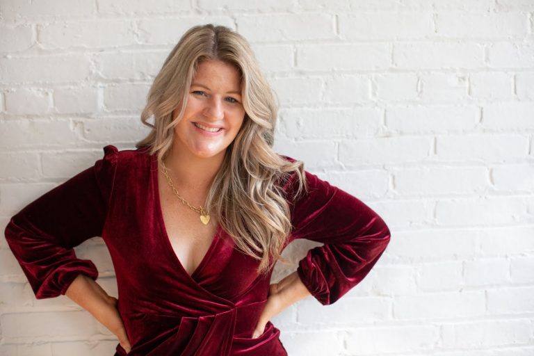 Libby Ward wearing a red dress standing in front of a white wall smiling