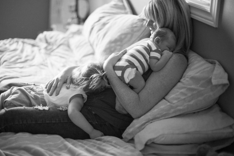Libby Ward lays in bed holding her new born sone with her daughter laying in her lap