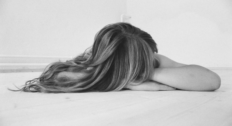 Woman struggling with motherhood mental health laying on the floor with hair covering face