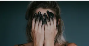 Woman puts her hands over her face, her fingers are all painted black