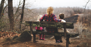 Mother and children sit on a wooden bench looking at nature