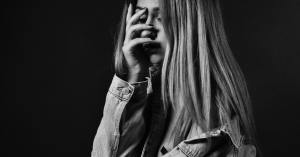 Black and white image of woman with hand over face representing mom guilt