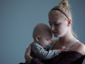 A tired mom holds a baby with a hand on his back. Sleep for Moms is important to prioritize