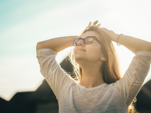 A woman wearing glasses looks to the sky with a slight smile on her face and sun setting in background
