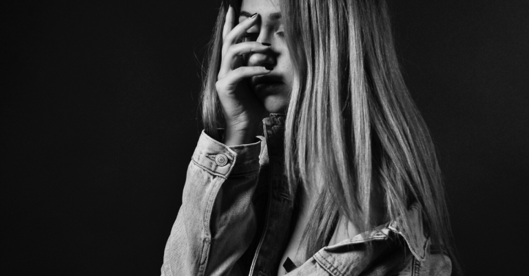 Black and white image of woman with hand over face representing mom guilt